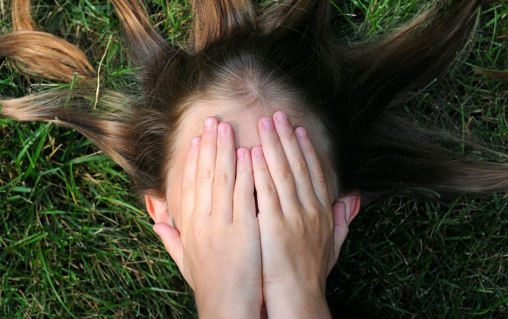 girl lying on grass with her hands covering her face