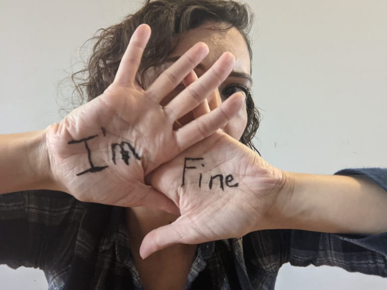 II'm fine is written on the palms of a woman's hands as she holds them up in front of her face